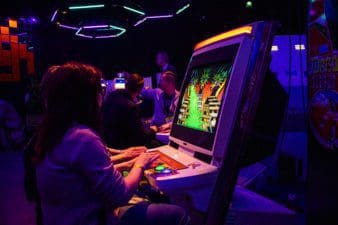 In a dark area lit by a variety of neon lights at Slush, a woman sits playing a retro arcade game.