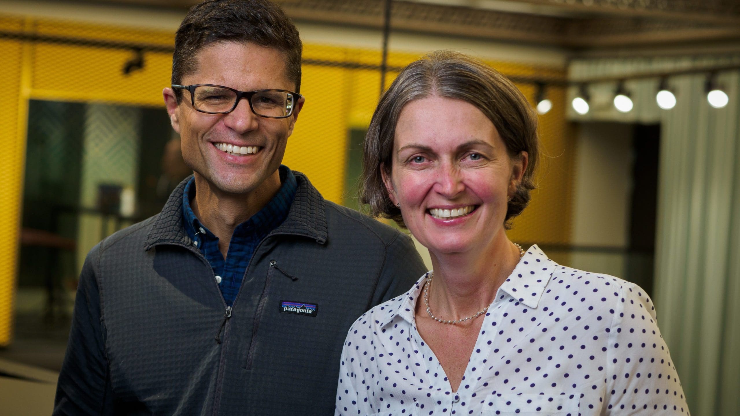 Autumn forest by Carmen Nguyen Ladi Carr & Sean Carr, both 90 Day Finn 2021 participants, stand together smiling at the camera in an office space, with a yellow wall situated in the background.