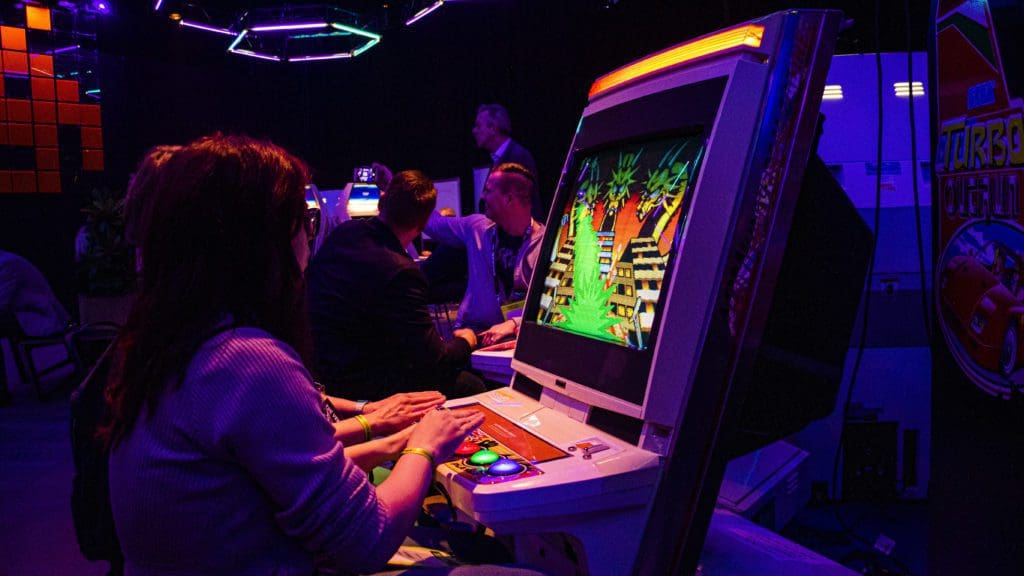 In a dark area lit by a variety of neon lights at Slush, a woman sits playing a retro arcade game.