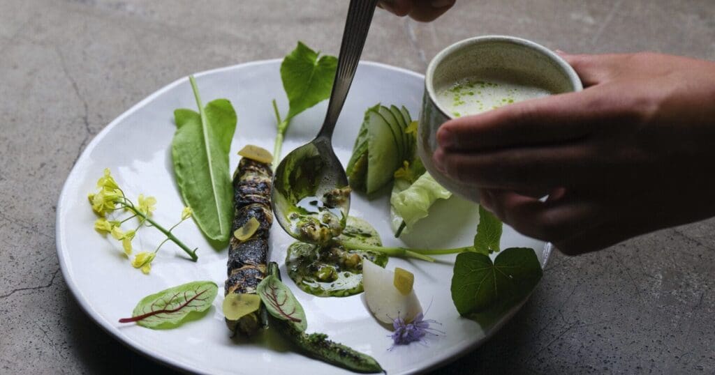 elicacy from restaurant Grön - Leek & pike "Roast", herbs from the Grön farm, grilled butter, mussel broth and parsley oil. Presented by Badass Food Stories in their piece, Farm-to-fork at Michelin-star restaurant Grön in Helsinki.